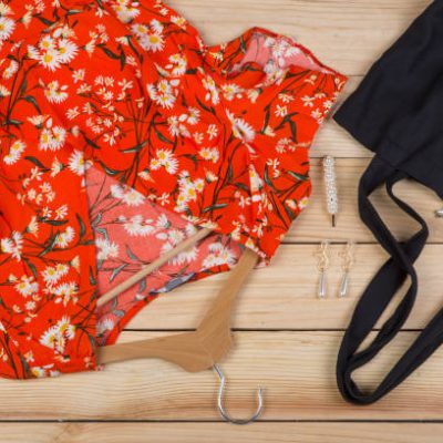 Fashion trends - black eco tote bag, dress in floral print on hanger and pearl jewelry: necklace, hair pearl clip, earrings on wooden desk